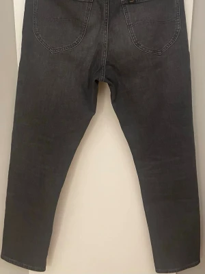 Mörkgrå Lee jeans med raka ben - Snygga mörkgrå jeans från Lee med raka ben och klassiska bakfickor. Jeansen har en diskret Lee-logga på bakfickan och svart patch i midjan. Perfekta för dig som gillar en clean och stilren look.