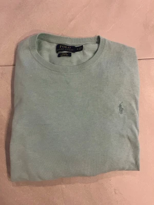 Ljusblå tröja från Polo Ralph Lauren - Snygg ljusblå tröja från Polo Ralph Lauren med klassisk rund halsringning och diskret broderad logga på bröstet. Tillverkad i mjukt material som känns skönt mot huden. Perfekt för dig som gillar stilrena och tidlösa plagg. Äkta!