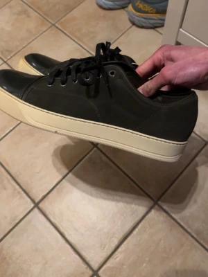 Mörkgröna sneakers från Lanvin - Snygga mörkgröna sneakers från Lanvin med vit sula och svarta skosnören. Ovandelen är i mocka och tån är i blankt material för en clean kontrast. Klassisk låg modell som passar till jeans eller chinos.