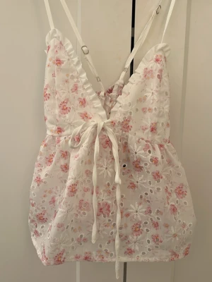 Blommig topp - Söt vit topp med rosa blommor och broderade detaljer. Djup v-ringning med volangkant och smala axelband som korsas i ryggen. Från Shein därav det billiga priset!