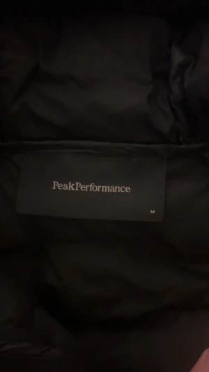 Svart pufferjacka Peak Performance M - Svart pufferjacka från Peak Performance i storlek M. Jackan har quiltad design, huva och dragkedja framtill. Perfekt för kalla dagar och har en clean look med diskret logga på bröstet. Ganska liten i storleken så passar er som har S i tröjor, knappt använd och är i fin kvalite.