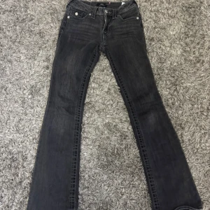 True Religion Becca Bootcut Jeans Svart - Svarta jeans från True Religion, modell Becca Mid Rise Bootcut. Snygga detaljer med kontrastsömmar och silverfärgade knappar på bakfickorna. Klassisk bootcut-passform och midwaist. Perfekt för dig som gillar en cool och tidlös look. Säljer för dom är för små, inget fel alls på dom!