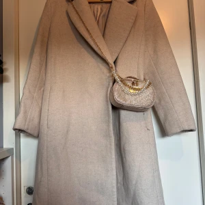 Beige kappa från H&M  - Snygg beige kappa från H&M med bred krage och klassisk rak passform. Jackan är helfodrad och har diskreta fickor i sidorna. Perfekt för dig som gillar stilrena och tidlösa plagg med en chill vibe.