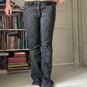 Grå bootcut jeans med broderi - Säljer ett par grå jeans med bootcut-passform och snyggt rosa broderi med texten 'Bootcut' på insidan av linningen. Jeansen har klassiska fem fickor och coola svarta detaljer på bakfickorna. Materialet är jeans och färgen är mörkgrå.
