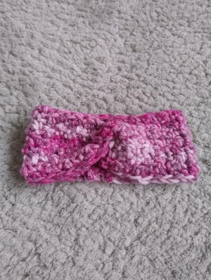 Rosa virkat pannband med twist - Säljer ett handgjort virkat pannband i olika nyanser av rosa och vitt som jag gjort själv. Pannbandet har en snygg twist framtill och är gjort i tjockt garn som ger en mysig och chunky känsla. Perfekt för att hålla öronen varma och ge din look lite extra färg.