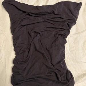 Grå t-shirt med rynkade sidor - Grå t-shirt i mjukt bomullsmaterial med rynkade detaljer längs sidorna. Klänningen har korta ärmar och en enkel, stilren design som ger en cool och avslappnad vibe. Perfekt för dig som gillar minimalistiskt och bekvämt.