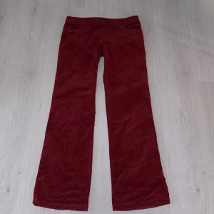 Vinröda manchesterbyxor Conte of Florence - Snygga vinröda manchesterbyxor från Conte of Florence i klassisk bootcut-modell. Byxorna har en diskret dragkedja i sidan och är tillverkade i mjuk manchester med raka ben. Perfekt för dig som gillar retrovibbar och vill sticka ut med färg.