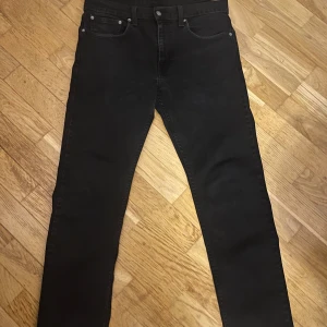 Svarta Levi's 502 jeans W32 L32 - Svarta jeans från Levi's modell 502 med klassisk femficksdesign och raka ben. Jeansen har en stilren look med svarta sömmar och diskret Levi's-märke på bakfickan. Perfekt för dig som gillar en enkel och clean stil.