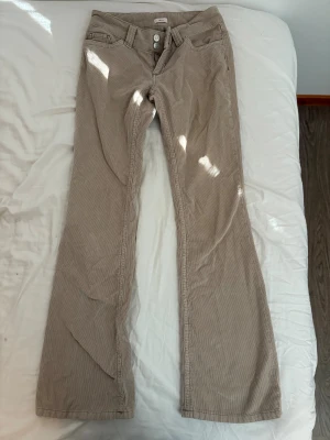 Beige manchesterbyxor med bootcut - Snygga beige manchesterbyxor från med bootcut passform och klassiska fickor fram. Byxorna har låg midja och stängs med två knappar och dragkedja brodering på bakfickorna.