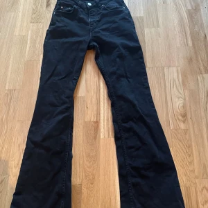 Svarta bootcut jeans från Perfect Jeans - Svarta jeans från Perfect Jeans med bootcut passform med normal midja. Klassisk femficksdesign, dragkedja och knapp framtill. Materialet är mjukt och stretchigt jeans, vilket gör dem riktigt sköna att bära. Perfekt för dig som gillar en snygg siluett och lite utsvängda ben.