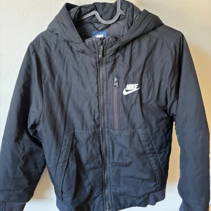 Svart jacka från Nike med huva - Svart jacka till barn från Nike med huva och dragkedja framtill. Storlek 8-10 år. 128-137 cm