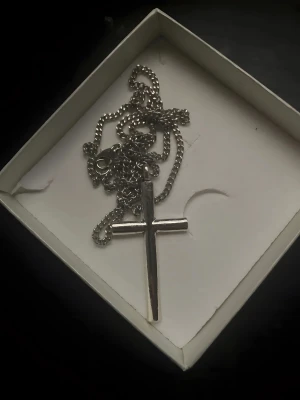 Kors halsband silver - Snyggt halsband med en klassisk korsberlock i silverfärgad metall. Kedjan är grov och har ett robust lås, perfekt för dig som gillar stilrena och tidlösa smycken. Passar till alla outfits och ger en cool touch till din look.