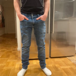 Replay Anbass ljusblå jeans slim fit -  ( Modellen är 173cm lång).     Säljer ett par Replay Anbass jeans i ljusblå tvätt med klassisk femficksdesign och snygga detaljer vid fickorna. Jeansen har slim fit-passning och är tillverkade i stretchigt jeanstyg för skön komfort. Perfekt för dig som gillar en modern och stilren look. Det är bara att slå en pling 🛎️ kring några funderingar