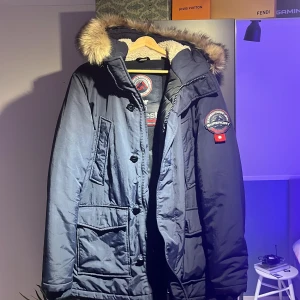   Superdry jacka  - Säljer en mörkblå Superdry Everest parkas med päls på huvan som går att ta av, stora fickor och patch på ärmen. Jackan har både dragkedja och knappar framtill samt mysigt teddyfoder inuti. Perfekt för kalla dagar. Använd fåtal gånger, priset är inte hugget i sten🙌