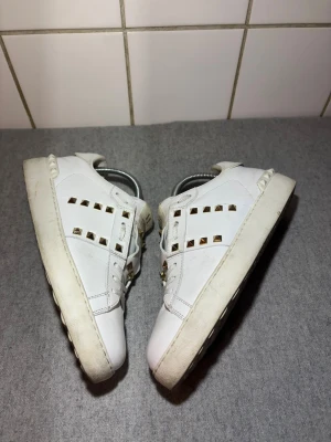 Valentino Open Rockstud Vit - Säljer ett par Valentino Open Rockstud i vitt med de ikoniska pyramidspikarna. Alla spikar sitter kvar och skorna är i mycket fint skick – endast lätt använda.  ✔ Storlek: 38,5 ✔ Modell: Open Rockstud ✔ Färg: Vit ✔ Skick: Mycket fint, minimalt slitage ✔ Tillbehör: Endast skorna (snören/box/påse medföljer ej)