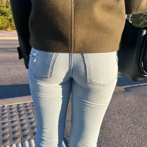 Ljusblå raka jeans - Säljer ett par ljusblå jeans med raka ben och slitna detaljer vid knän och fickor. Jeansen har klassisk femficksdesign, mid midja och fransade benslut för en cool vibe. 