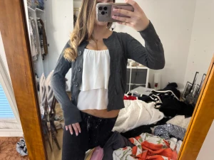 Mörkgrå kofta från H&M med knappar - Snygg mörkgrå kofta från H&M i storlek M. Koftan har långa ärmar, rund hals och stora knappar framtill. Enkel och stilren design som funkar till många outfits.