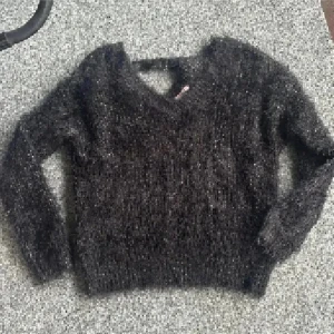 Svart fluffig stickad tröja Sincerely Loved - Mysig svart stickad tröja från Sincerely Loved med fluffig yta och glittriga inslag. Tröjan har v-ringad hals, lång ärm och en loose passform som ger en chill vibe. Perfekt för att hålla sig varm och ändå se cool ut. Glitter på 😊💕