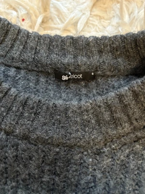 Grå stickad tröja från Gina Tricot - Mysig grå stickad tröja från Gina Tricot i storlek S. Tröjan har ribbade muddar vid hals, ärmslut och nederkant, samt en klassisk rund halsringning. Perfekt för kyliga dagar och enkel att matcha med jeans eller kjol.