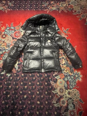 Moncler Montbeliard - Säljer min Moncler Montbeliard. Jackan har quiltad design, dragkedja med rödvit detalj, flera fickor och lång ärm. Materialet är glansigt och känns riktigt lyxigt, perfekt för kalla dagar.