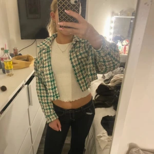 Grön och vit rutig croppad overshirt - Säljer en croppad overshirt med grön och vit rutig design. Jackan har klassisk krage, långärmade ärmar och är tillverkad i ett tjockare, stickat material som ger en cool och trendig look. Perfekt att styla med jeans och topp för en snygg outfit.