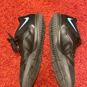 Nike Tiempo Legend 9 Academy IC Renew - Svart/Grå  - Nike Tiempo Legend 9 Academy IC Renew inomhusskor i svart färg med ljusblå och guldgrå detaljer. Dessa skor är designade för att ge bra bollkontroll och ökad precision. Yttersulan i gummi är utformad för grepp i flera riktningar på inomhusytor. Ovandelen har upphöjda texturer med mjuka skumkuddar för exakt dribbling, passning och skott.   Ovandelen är i KALVSKINN vilket formar sig efter foten och har god andningsförmåga. 