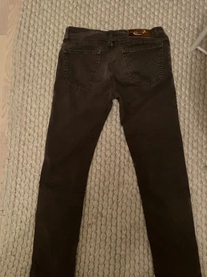 Bruna byxor från Jacob Cohen - Snygga bruna byxor från Jacob Cohen i mycket bra skick. Byxorna har raka ben och är tillverkade i ett mjukt bomullsmaterial med detaljerade sömmar och silverfärgade knappar. Perfekta för dig som gillar stilrena och unika plagg.