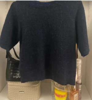 Mörkblå stickad tröja med kort ärm - Säljer en mörkblå stickad tröja med korta ärmar och rund hals. Tröjan har en mjuk och lite luddig yta som ger en mysig känsla. Perfekt för dig som gillar enkel och stilren design med en chill vibe.