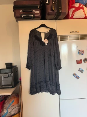 Svart Odd Molly klänning med spets - Supersnygg grå klänning från Odd Molly med hjärtformade prickar, spetsdetaljer vid halsen och volangkant nedtill. Långärmad modell med lätt v-ringning och mjukt, flowy tyg som ger en chill vibe. Perfekt för dig som gillar unika detaljer och romantisk stil. Storlek 4 som enligt deras storleksguide motsvarar en L/XL. Helt ny med tags. 