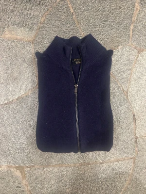 Mörkblå kofta från Massimo Dutti - Mörkblå kofta från Massimo Dutti i en mix av ull och kashmir. Modellen har hel dragkedja framtill, ribbade muddar och hög krage. Perfekt för lager-på-lager och riktigt skön att bära under kyliga dagar. Liten skade på dragkedje kanten längst ner (bild 3). Nypris: 1399 