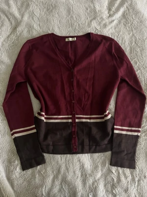Kofta - Snygg kofta i vinrött och mörkbrunt från Flash Basic. Modellen har v-ringning, knappar hela vägen och långa ärmar. Perfekt att slänga över en t-shirt eller linne. Vintage liknande, ger gryffindor / Harry Potter vibes. Är i storlek M men passar som S.