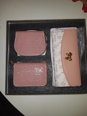 Set med plånböcker från Fankaru - Snyggt set med två rosa plånböcker i croco-mönstrad syntet och en större plånbok i beige och rosa med tryckt logomönster och guldfärgad rosett. Perfekt för att hålla koll på kort, cash och smågrejer. Stilren design som passar dig som gillar detaljer.