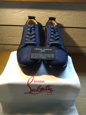 Mörkblå sneakers Christian Louboutin - Snygga mörkblå sneakers från Christian Louboutin med klassisk snörning och rund tå. Ovandelen är i mocka och insidan har en beige ton. Sulan är röd med Louboutin-logga, vilket ger en exklusiv vibe. Perfekt för dig som vill sticka ut med stilrena och lyxiga skor.