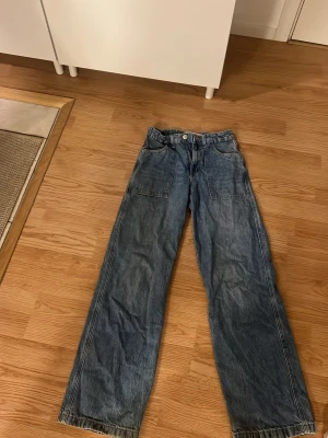 Blå wide leg jeans 152cm - Säljer ett par blå wide leg jeans med raka, vida ben och stora fickor fram. Klassisk denimlook med snygga sömmar och normal midja. Perfekta för dig som gillar avslappnad stil och vill ha bekväma jeans med lite extra utrymme.