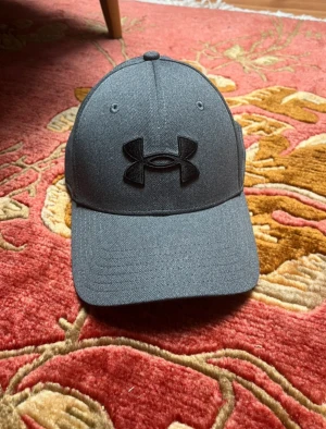 Grå keps från Under Armour S/M - Snygg grå keps från Under Armour, kepsen aldrig amvänd så skicket är 10/10. Storlek S/M