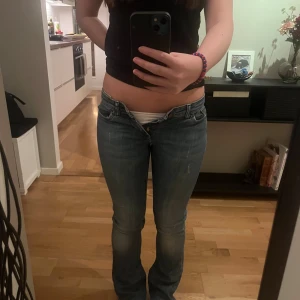 Lågmidjade blå jeans från Lee - Säljer ett par blå jeans från Lee med låg midja och klassisk femficksdesign. Jeansen är bootcut och Lee-logga på bakfickan. Materialet är jeans med snygga kontrastsömmar och dragkedja framtill.