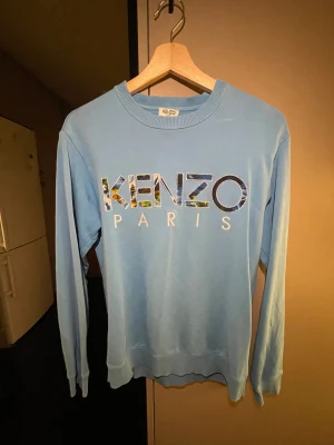Kenzo sweatshirt - Ljusblå sweatshirt från Kenzo. Perfekt för dig som vill sticka ut lite extra. Har använt under några månader förra året annars har den bara tagit plats i min garderob. Ny pris 2000kr
