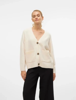 Beige kofta med knappar och fickor - Säljer en beige kofta med djup v-ringning, stora bruna knappar och två rejäla fickor framtill. Koftan har lång ärm och är stickad i mjukt material, perfekt för lager-på-lager. Enkel och clean look som funkar till många stilar.