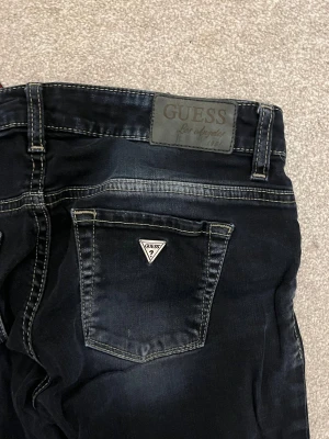 GUESS jeans - Snygga mörkblå skinny jeans från Guess med slitningar och tydliga kontrastsömmar. Klassisk femficksmodell med Guess-logga på bakfickan och läderpatch i midjan. Jeansen har låg midja.