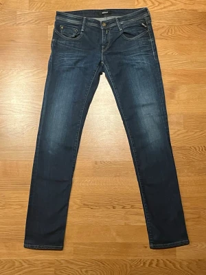 Replay jeans W28 L32 - Snygga mörkblå jeans från Replay med klassisk femficksdesign och smal passform. Jeansen har subtila slitningar och kontrastsömmar, tillverkade i stretchig denim för extra komfort. Perfekta för dig som gillar en stilren och modern look.