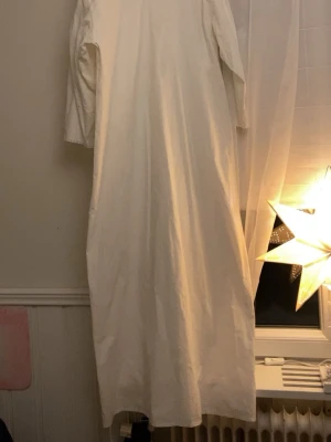 Vit långklänning med v-ringning/ lucia klänning  - Enkel och stilren vit långklänning med v-ringad hals och långa ärmar. Klänningen har en rak och lös passform, perfekt för dig som gillar minimalistisk stil. Tillverkad i ett mjukt tyg som känns skönt mot huden.