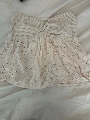 Beige tubtopp med broderade blommor - Supersöt beige tubtopp med virkad överdel och broderade blommor i spets på den nedre delen. Toppen är axelbandslös och har en bandeauformad passning som sitter snyggt. Perfekt för sommarens alla häng och festivaler!