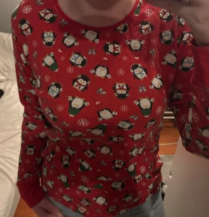 Röd långärmad pjamas med pingvinmönster - Säljer en röd långärmad tröja med gulligt pingvinmönster och snöflingor över hela. Perfekt för dig som vill ha en mysig och rolig look under vintern eller julen. Tröjan har rund hals och är gjord i mjukt material som känns skönt mot huden.