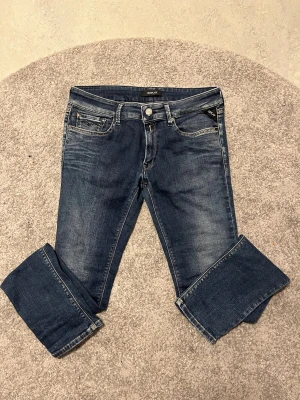 Mörkblåa Replay jeans - Snygga mörkblå jeans från Replay med klassisk femficksdesign. Jeansen har slitningar och kontrastsömmar, samt Replay-logga på knapp och ficka. Materialet är robust denim med en skön känsla. Den passar perfekt för någon mellan 164-170cm. Jeansen är helt oanvända och helt nya. De har aldrig använts heller så de finns ingen syn på användning.
