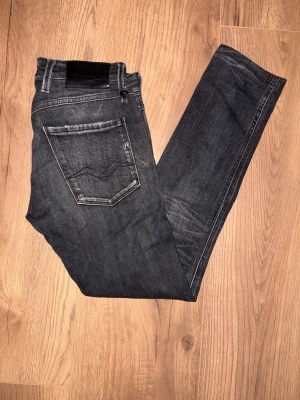 Replay Anbass svarta skinny jeans - Säljer ett par Replay Anbass jeans i mörkgrått med slitningar och skinny passform. Jeansen har klassiska fem fickor, snygga detaljer på bakfickorna och är tillverkade i stretchigt denim för skön komfort. Perfekt för dig som gillar en smal siluett.