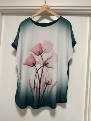 Blommig topp från J&X Fashion - Säljer en loose-fit topp från J&X Fashion med blommigt mönster i rosa och paljettdetaljer framtill. Toppen har korta ärmar, rund hals och en snygg gradient från mörkgrön till vit. Materialet är mjukt och lätt polyester, perfekt för vår och sommar. Helt NY!