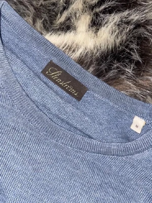 Blå merinoulltröja från Stenströms - Snygg blå stickad tröja från Stenströms i storlek M, tillverkad i 100% merinoull. Tröjan har rund hals och långa ärmar, med ribbade muddar vid hals, ärmslut och nederkant. Perfekt för dig som gillar klassisk och stilren design.