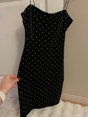 Svart sammetsklänning med strass H&M - Supersnygg svart sammetsklänning från H&M med tunna axelband och täckt av små glittriga strassdetaljer. Kort modell med figurnära passform. I toppenbra skick!