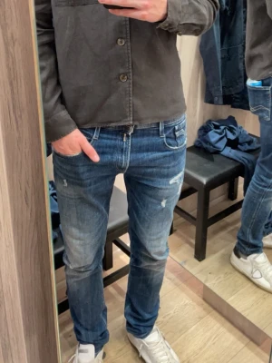 Replay Anbass slim fit jeans - Snygga Replay Anbass jeans i slim fit med klassisk femficksdesign. Jeansen är blå med lätt slitna detaljer och har dragkedja i gylfen. Materialet är mjukt jeans-tyg och passformen är smal men bekväm. Perfekta för dig som gillar stilrena och moderna jeans.