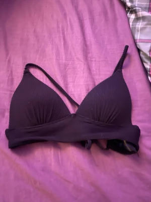 Svart ribbad bikiniöverdel från H&M - Säljer en svart bikiniöverdel från H&M i storlek 34. Den har ribbad struktur, smala axelband och en enkel, stilren design. Perfekt för dig som gillar minimalistisk stil på stranden eller vid poolen.